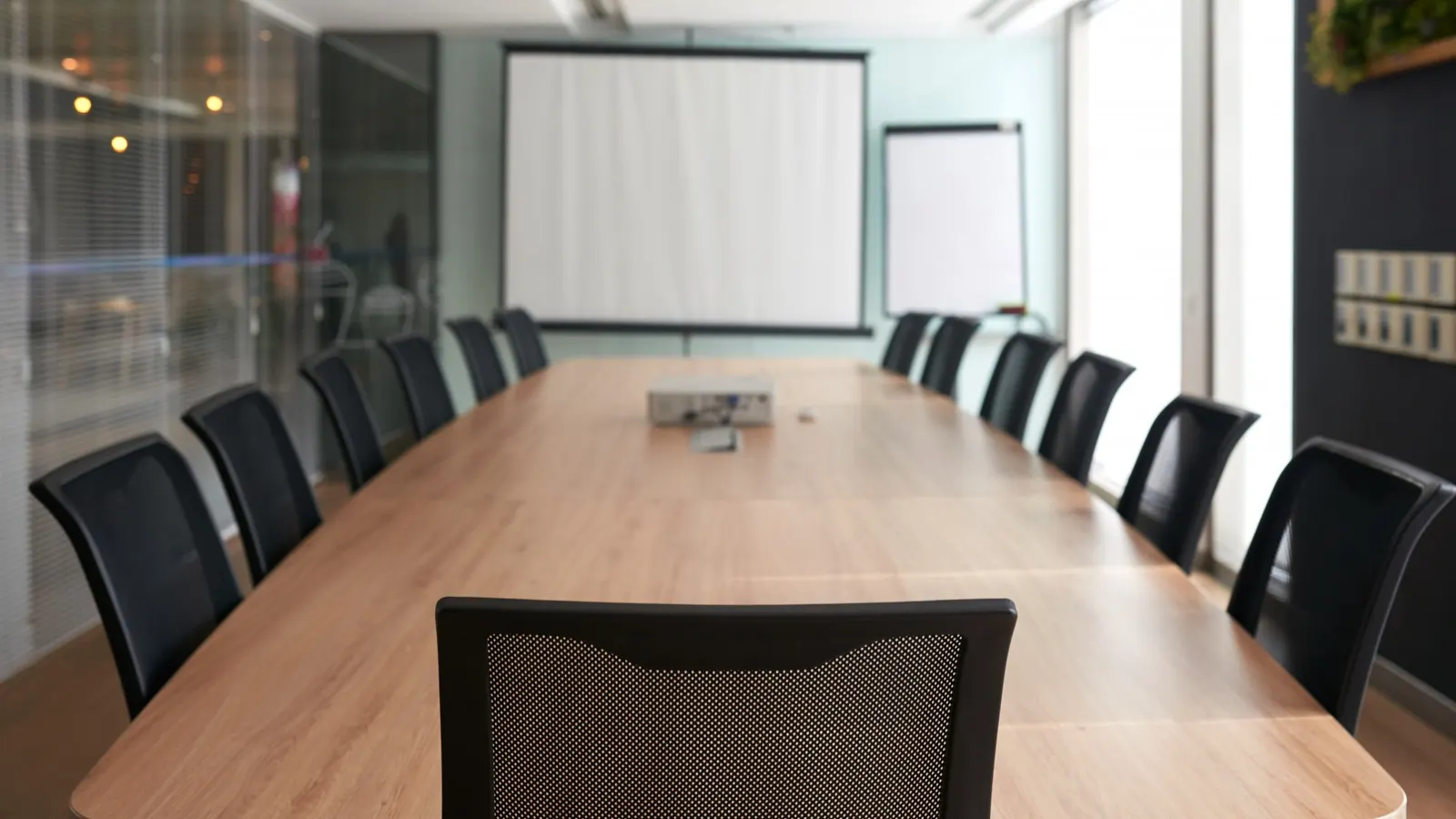 Empty meeting room with a long wooden table, black chairs, a projector screen and a flip chart
